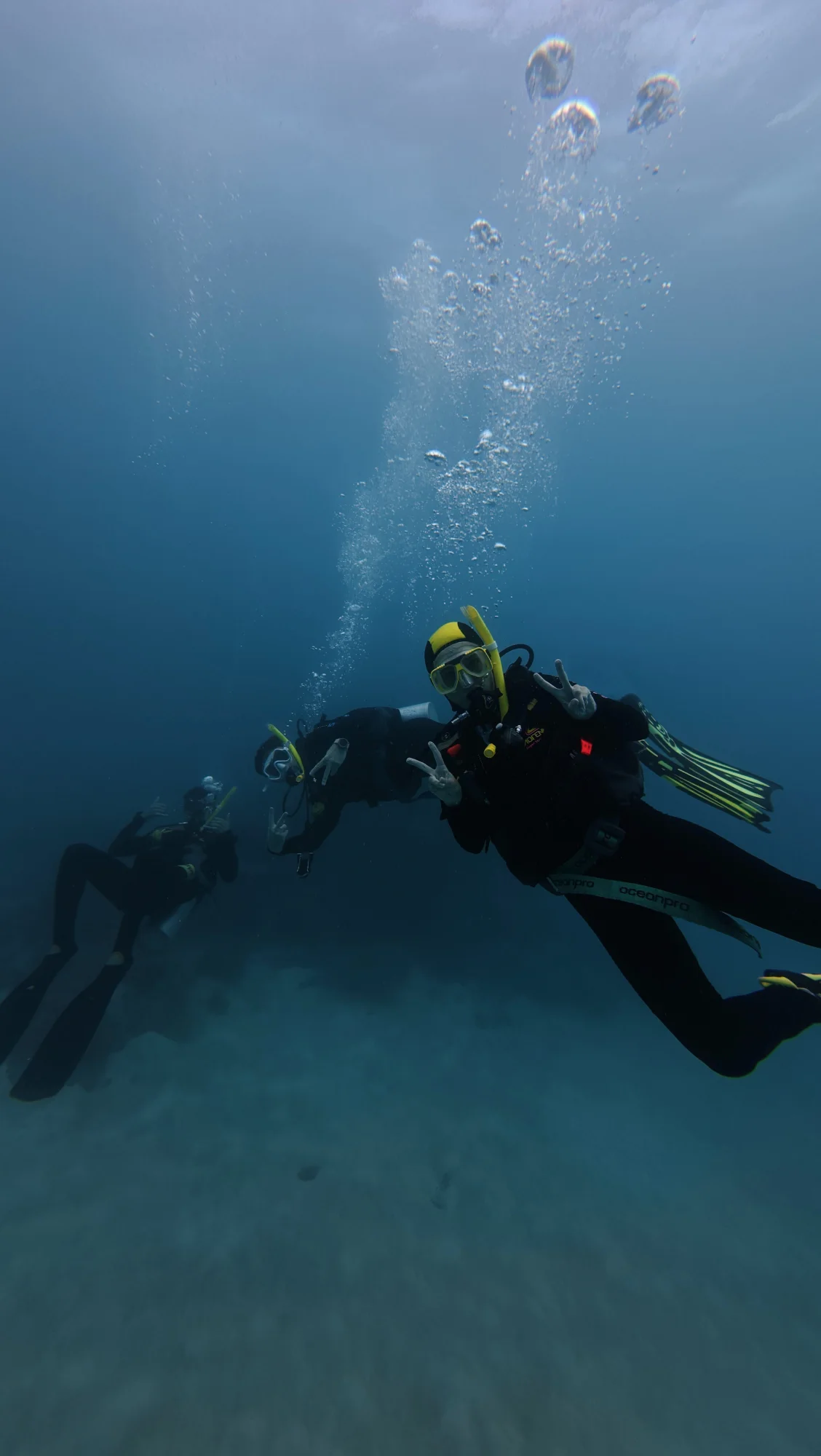 Three scuba divers suspended in open water beneath rising bubbles